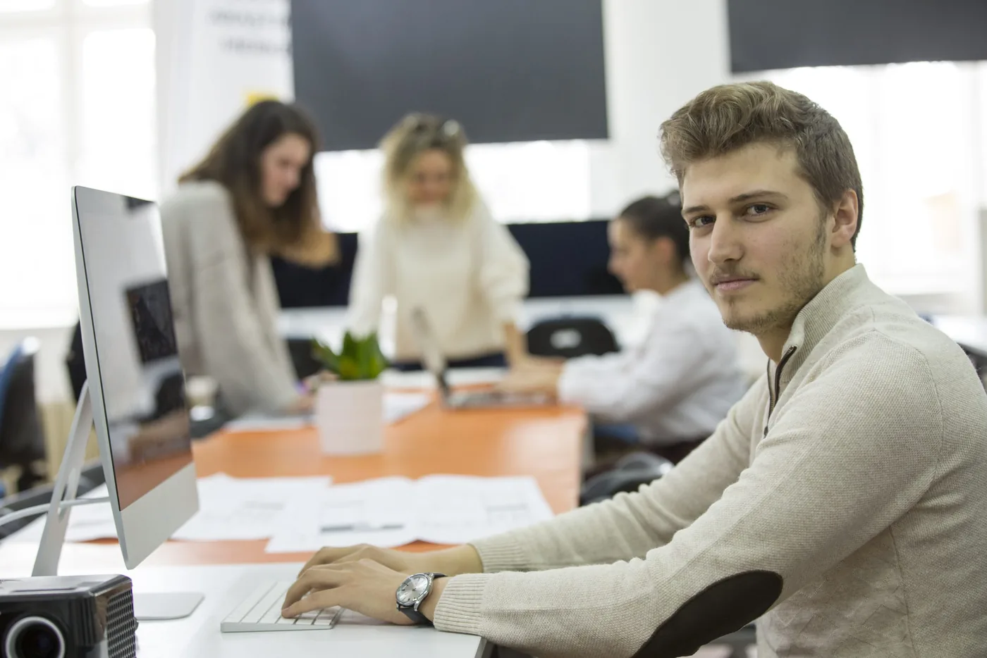 Employee at a desk in an open-plan office with colleagues in the background