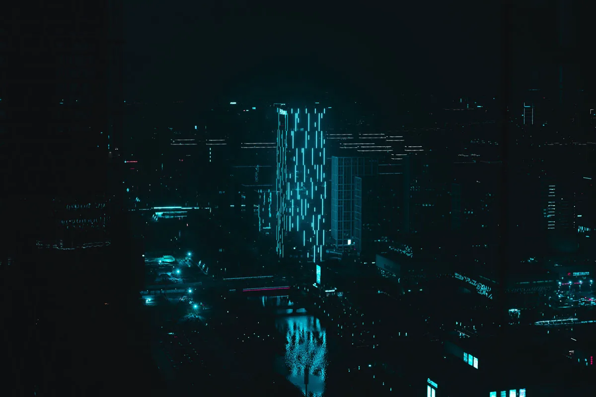 Perfil urbano nocturno visto desde arriba, con líneas de luz azul en una torre
