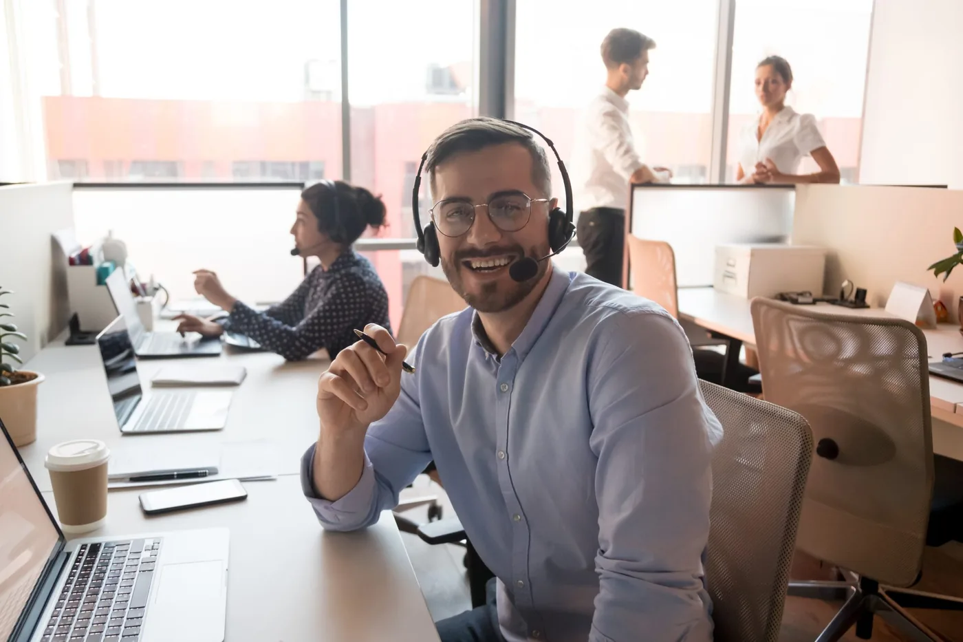 Agent de service desk avec un casque et un stylo à la main à un bureau avec des portables