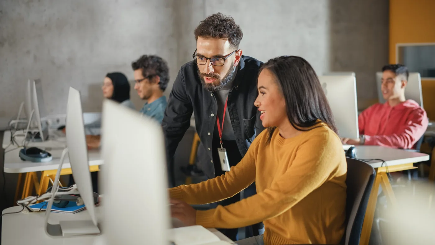 Colleague looking over the shoulder of someone at a monitor in an open-plan office
